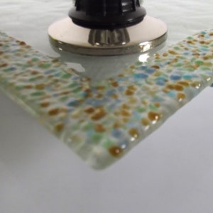 May include: A close-up of a glass tray with a speckled design in shades of blue, green, and brown. The tray has a smooth, rounded edge.