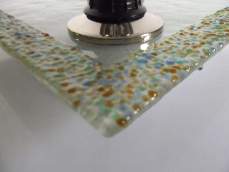 May include: A close-up of a glass tray with a speckled design in shades of blue, green, and brown. The tray has a smooth, rounded edge.
