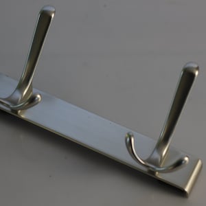 May include: A silver metal hook rack with two double hooks. The rack is designed to be mounted on a wall.