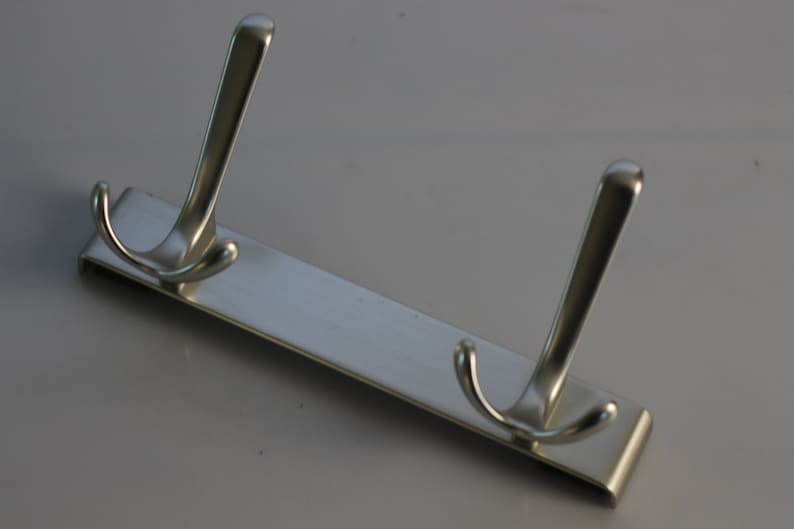 May include: A silver metal hook rack with two double hooks. The rack is designed to be mounted on a wall.