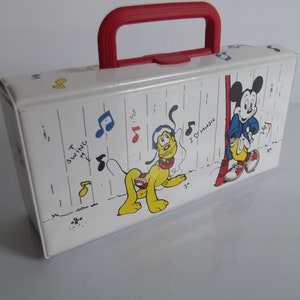 May include: A white plastic carrying case with a red handle. The case features a cartoon image of Mickey Mouse and Pluto with musical notes and the text "I love music" and "To swing with".
