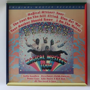 以下が含まれることがあります： ビートルズの「Magical Mystery Tour」のアルバムカバーアートを額装。カラフルなアートワークは、コスチュームを着たバンドメンバー、曲名、アルバムタイトルが特徴です。フレームはマルチカラーのボーダーです。