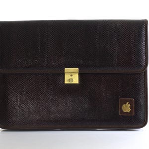 May include: A brown leather briefcase with a gold clasp and an Apple logo.