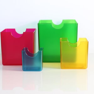 May include: Four clear plastic containers in different sizes and colours: red, green, blue, and yellow. The containers have a unique design with a cut-out section at the top.