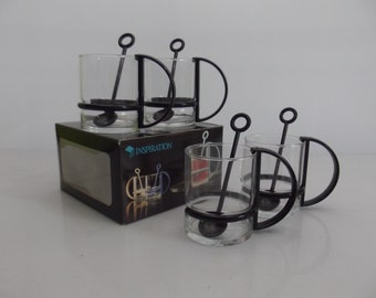 Op de afbeelding: Set van vier glazen glazen met zwarte handvatten en bijpassende zwarte roerlepels. De glazen zijn verpakt in een zwarte doos met het woord "INSPIRATION" erop gedrukt.