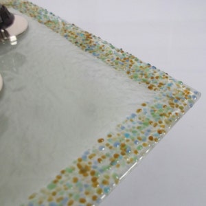 May include: A white glass light fixture with a square shape and a border of small, colorful glass beads. The beads are in shades of blue, green, and gold.