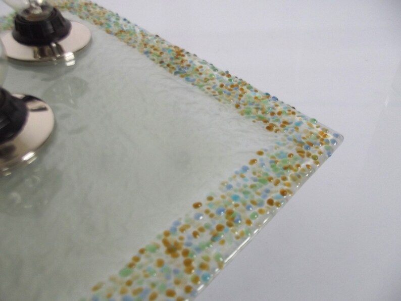 May include: A white glass light fixture with a square shape and a border of small, colorful glass beads. The beads are in shades of blue, green, and gold.