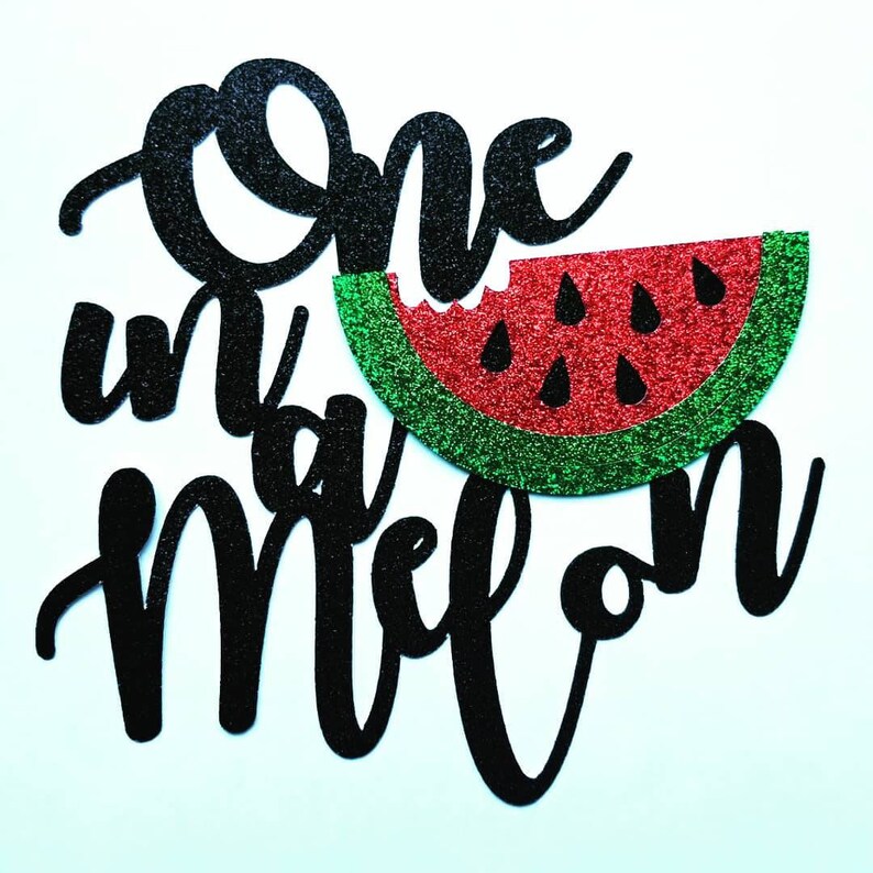 Op de afbeelding: Een zwarte glitter taarttopper met de tekst "One in a melon" in een sierlijk lettertype. Het ontwerp bevat een rood en groen glitter watermeloen plakje met een hap eruit.