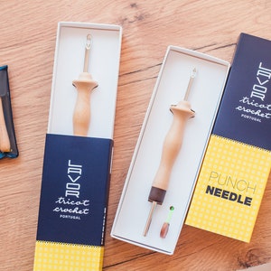 Pu&ograve; includere: Tre scatole contenenti strumenti per la punzonatura. Le scatole sono blu e gialle con il testo "Tricot Crochet Portugal" e "Punch Needle".