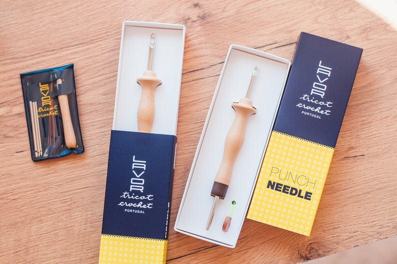 Pu&ograve; includere: Tre scatole contenenti strumenti per la punzonatura. Le scatole sono blu e gialle con il testo "Tricot Crochet Portugal" e "Punch Needle".