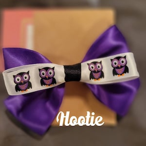 May include: Purple satin bow with a white ribbon featuring four purple owls. The ribbon has the text "Hootie" printed on it.