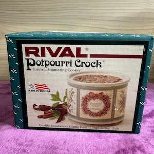 Peut inclure: Une boîte de produit rectangulaire pour un mijoteur électrique Rival Potpourri Crock. La boîte présente une bordure sarcelle avec des motifs de feuilles blanches et une image centrale d'un pot en grès orné d'une couronne florale et de bâtons de cannelle.