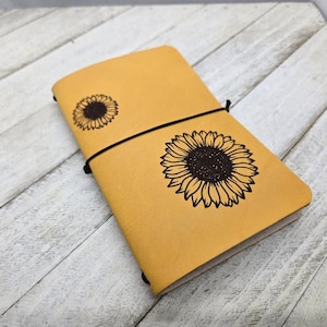 May include: A yellow leather journal with a black elastic closure and two sunflower designs.