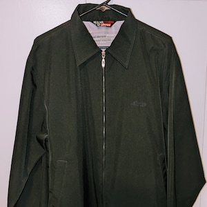 May include: A dark green jacket with a zipper closure and a small logo on the left chest. The jacket has a  "Lost Jacket" label on the collar.
