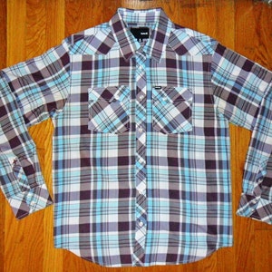 May include: A long-sleeved plaid shirt with a blue, white, and brown pattern. The shirt has a button-down collar and two chest pockets.