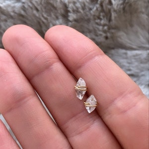 Könnte beinhalten: Ein Paar kleine, klare Quarzkristall-Ohrringe mit goldener Drahtwicklung. Die Kristalle sind diamantförmig und in einem schlichten, minimalistischen Stil gehalten.
