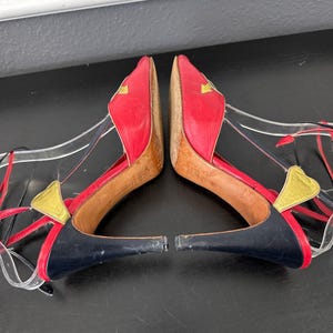 May include: Pair of red and black high-heeled shoes with a unique design. The shoes feature red leather uppers with gold accents, black heels, and clear straps. The heels are approximately 3 inches (7.6 cm) high.