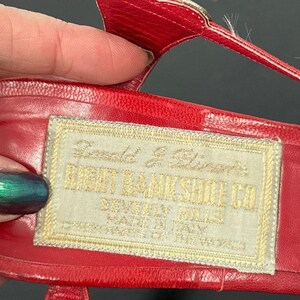 May include: Close-up of a red leather sandal with a gold buckle. A rectangular label with gold text reads "RIGHT BANK SHOE CO. BEVERLY HILLS MADE IN ITALY". The sandal is likely vintage.