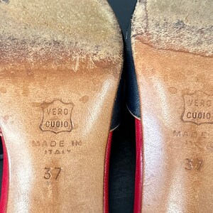 May include: Close-up of the soles of two shoes. The soles are brown leather with the text "VERO CUOIO" and "MADE IN ITALY" stamped on them. The number "37" is also visible. The shoes have red and navy blue accents.