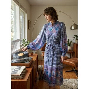 May include: A patterned dress in blue and purple tones with long sleeves and a tie waist. The dress has a high neckline and a flowing skirt. The sleeves are balloon-shaped. A woman is near a record player.