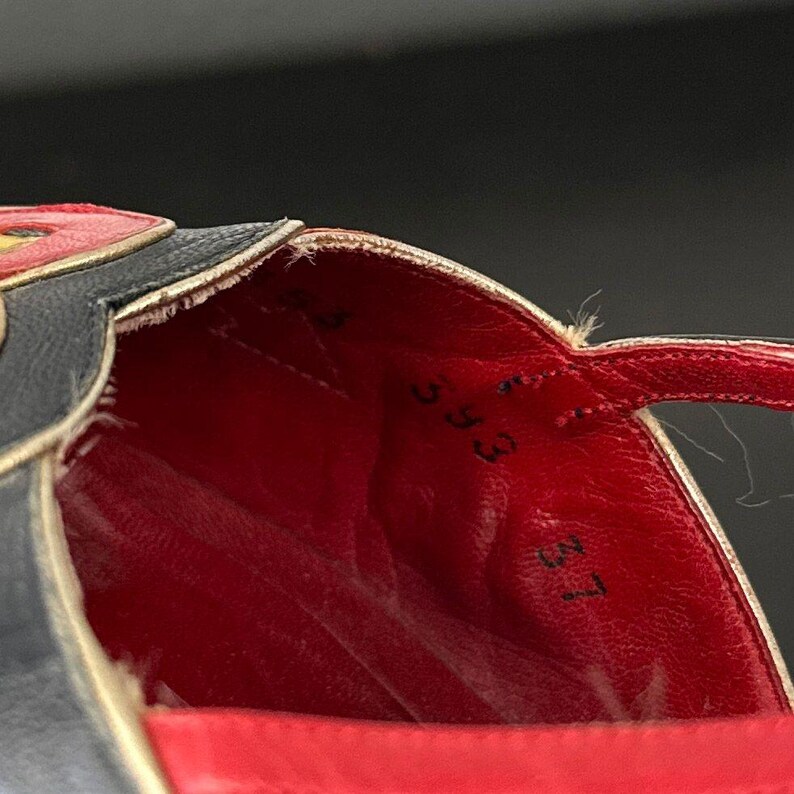 May include: Close-up of a black and red sandal. The interior is red, with black numbers printed on the insole. The sandal has a strap and a decorative design on the upper.