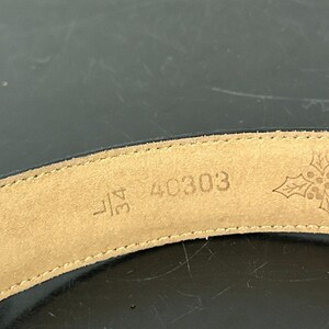 May include: Close-up of a black belt with a tan leather interior. The interior displays the size 34L, the number 40303, and a snowflake design. The belt is curved and appears to be made of leather.