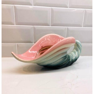 May include: A ceramic seashell planter in shades of pink, white, and blue. The planter is shaped like a seashell with a curled lip.
