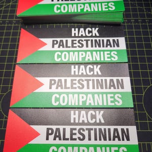 May include: Rectangular stickers with the text "HACK PALESTINIAN COMPANIES" in white, black, and green. The design incorporates the Palestinian flag colors and a triangular element. A stack of similar stickers is visible.