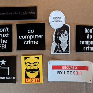 Peut inclure: Une collection d'autocollants avec différents motifs et textes. Les autocollants sont en noir et blanc avec quelques accents rouges et jaunes. Le texte sur les autocollants comprend "The Secret ingredient is cybercrime", "Don't Trust The FBI", "do computer crime", "SORRY AMON, I ONLY LIKE BOYS WHO DO CYBERCRIME", "COME AND TAKE IT", "FSOCIETY", "don't do computer crime", et "SECURED BY LOCKBIT".