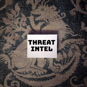 May include: A rectangular white card featuring the bold black text THREAT INTEL centered on its surface. The card is positioned against a dark blue and beige fabric background that displays a repeating pattern of a mythical creature with a collar.