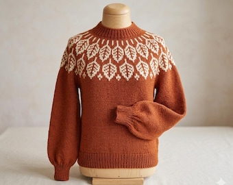 May include: Rust-colored sweater with a white leaf pattern across the yoke. The long sleeves have a slight puff at the shoulder and a ribbed cuff. The sweater is displayed on a wooden mannequin.