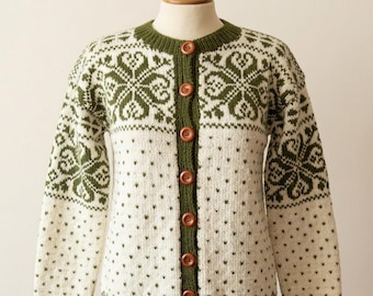 May include: Cream-colored cardigan with a green floral pattern and trim. The button-down sweater features a round neckline and long sleeves. The design includes a series of green floral motifs and small dots, with wooden buttons down the front.