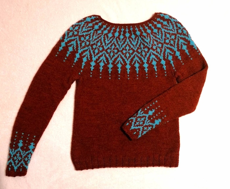 Pu&ograve; includere: Un maglione bordeaux a maniche lunghe e girocollo. Il maglione presenta un motivo geometrico turchese sulle spalle, sui polsini e sulla parte superiore del petto. La maglia &egrave; di colore pieno con un design dettagliato.