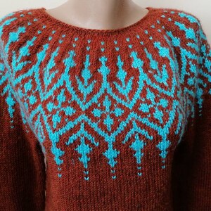 Pu&ograve; includere: Un maglione color ruggine con un motivo geometrico turchese sul petto e sulle spalle. Il maglione a maniche lunghe ha uno scollo tondo ed &egrave; realizzato in materiale a maglia. Il design turchese &egrave; simmetrico e presenta un motivo ripetuto.