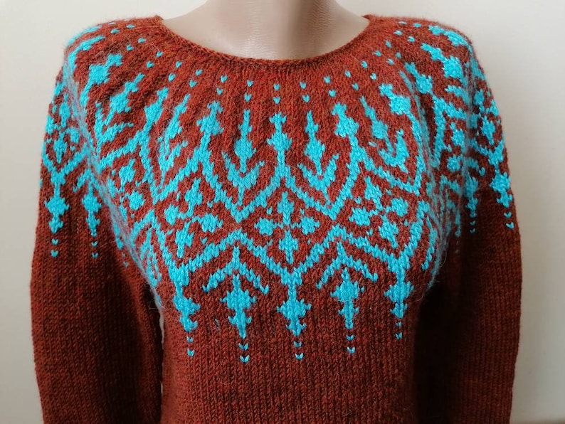 Pu&ograve; includere: Un maglione color ruggine con un motivo geometrico turchese sul petto e sulle spalle. Il maglione a maniche lunghe ha uno scollo tondo ed &egrave; realizzato in materiale a maglia. Il design turchese &egrave; simmetrico e presenta un motivo ripetuto.