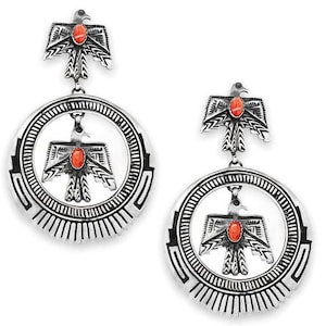Puede incluir: Un par de pendientes de plata con un diseño circular que presenta un águila estilizada con una piedra roja en el pecho. Los pendientes son de estilo colgante con un pequeño amuleto de águila en la parte superior.