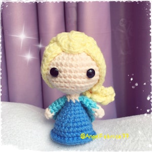May include: A crocheted doll with a yellow braid, blue dress, and light blue accents. The doll has a pink face with black eyes and a small, pink nose.