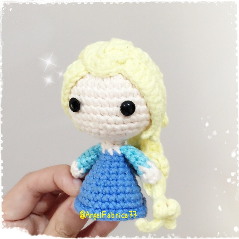 May include: A crocheted doll with a light blue dress, white and light blue sleeves, and long yellow hair. The doll has black eyes and a pink face.
