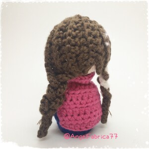 May include: A crocheted doll with brown hair in braids, wearing a pink sweater and blue jeans. The doll is facing away from the camera.