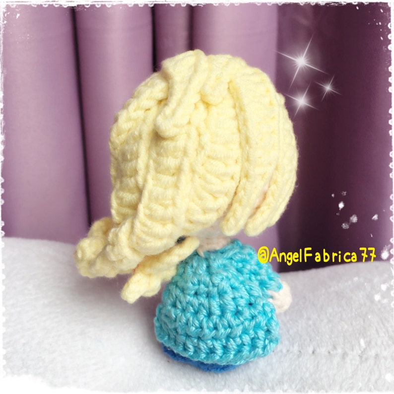 May include: A crocheted doll with long blonde hair and a blue dress. The doll is facing away from the camera.