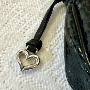 Op de afbeelding: Een zwarte leren handtas met een zilveren hartvormige hanger met daarop "Brighton".