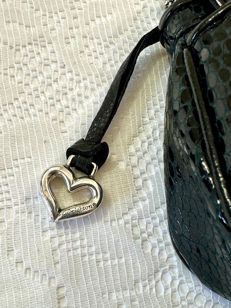 Op de afbeelding: Een zwarte leren handtas met een zilveren hartvormige hanger met daarop "Brighton".