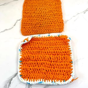 May include: Two orange crocheted dishcloths. One dishcloth has a white and blue crocheted border.