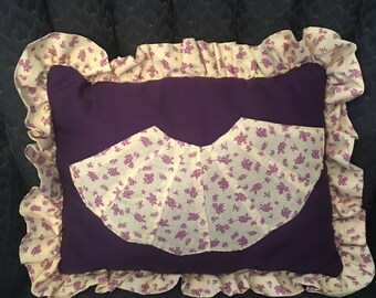 May include: A purple pillow with a white and purple floral print. The pillow has a ruffled edge and is made of a soft fabric.