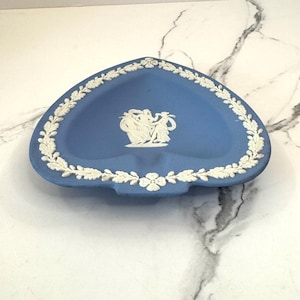 May include: A blue and white heart-shaped ceramic dish with a white floral design around the edge and a white cameo of three women dancing in the center.