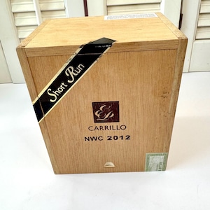 May include: A wooden box with a light brown finish. The box has a black label that reads "Short Run." The box also has the text "Carrillo NWC 2012" printed on it. A small green sticker is on the bottom right corner.