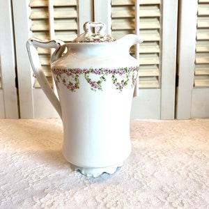 May include: White porcelain creamer with a floral design featuring pink roses and green leaves. The creamer has a gold-trimmed handle and a scalloped base.