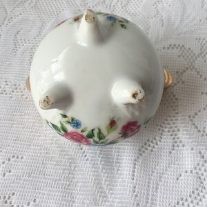 May include: White ceramic trinket dish with a floral design in pink, blue, and green. The dish has three gold feet and a rounded shape.
