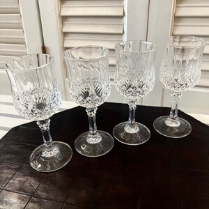 May include: Four clear glass wine glasses with a diamond pattern on a black and white checkered surface.