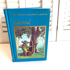 May include: A blue hardcover book with gold lettering titled "The Weekly Reader Classics Robin Hood". The cover features an illustration of Robin Hood and his men in the forest.